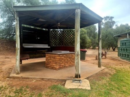Seating and barbeque with brick sides under a pine post partially closed veranda.