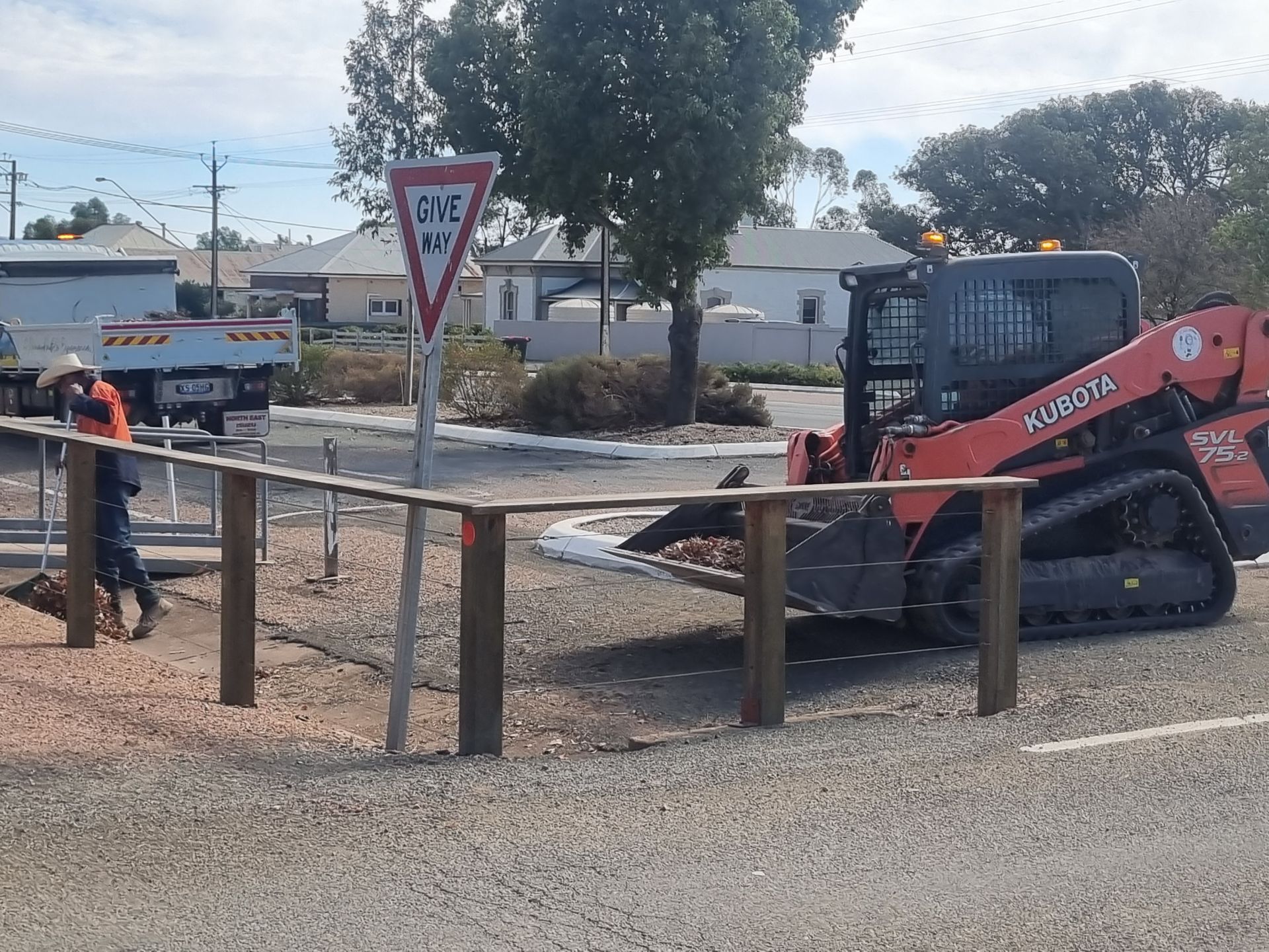 Skidsteer assisting worker in clean up of leaves in a gutter.