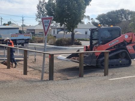 Skidsteer assisting worker in clean up of leaves in a gutter.