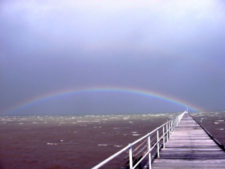 View over dark sea, rainbow over end of Port Germein Jetty.