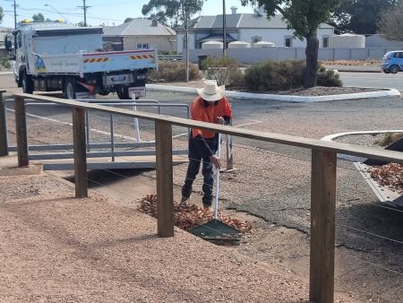 Council worker raking leaves out of a gutter.